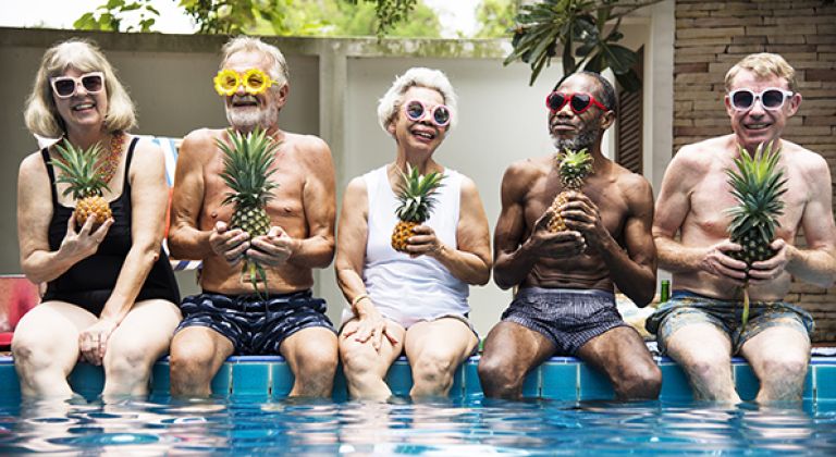 Group of people sitting on edge of swimming pool holding pineapples
