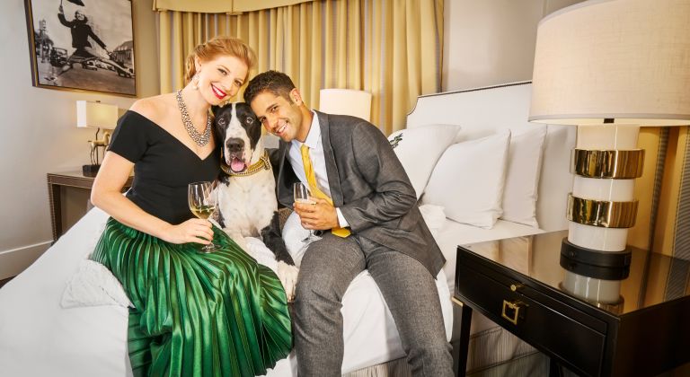 A Man And A Woman sitting on bed with a dog.