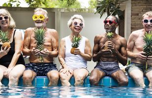Group of people sitting on edge of swimming pool holding pineapples