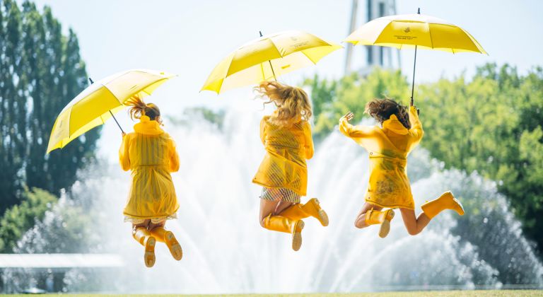 Three people jumping in the air while holding yellow umbrellas